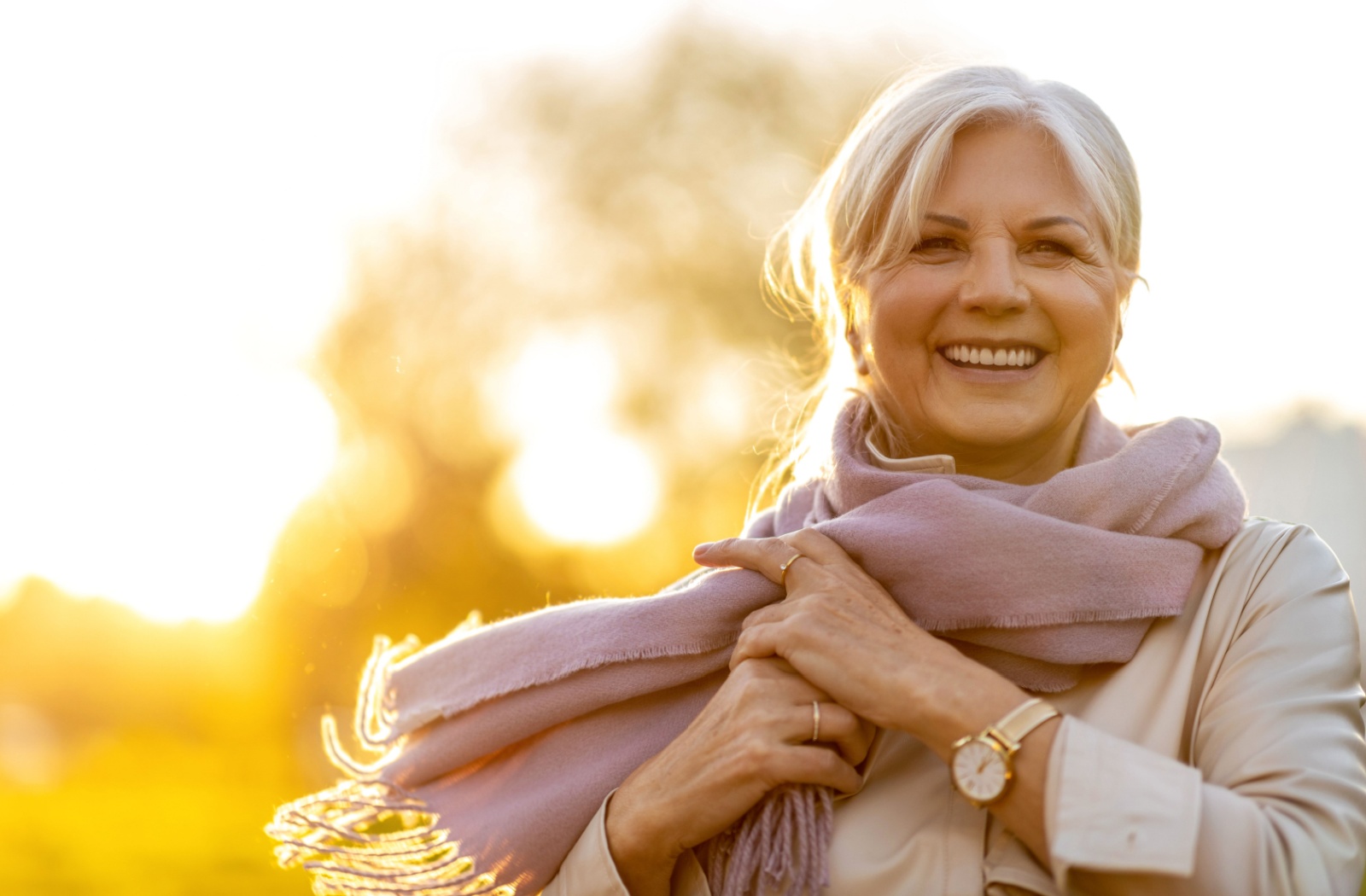 Older person with a pink scarf smiles blissfully into the setting sun.
